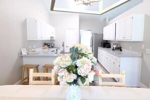A modern kitchen with white cabinets, a central island, and a dining area with a wooden table and chairs.