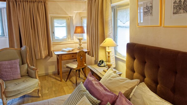 A hotel room with a bed, a desk, a chair, a lamp, and a window with curtains. - The LITTLE WOLF***** - A balcony over the garden (Riquewihr)