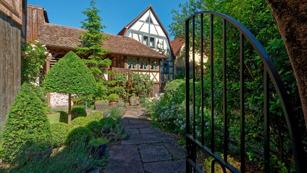 A traditional half-timbered house with a stone pathway leading to a gated entrance.