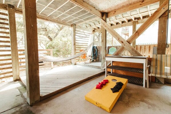 A wooden deck with a hammock, a table with benches, and a yellow board game.
