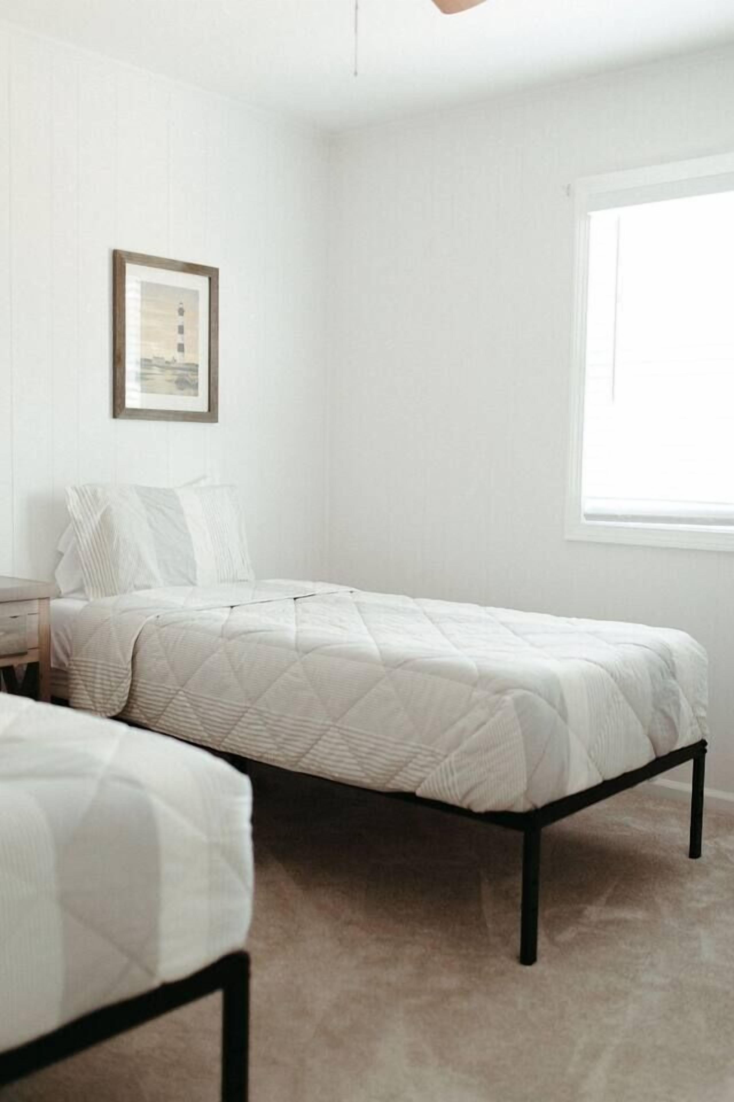 A bedroom with two beds, a framed picture on the wall, and a window providing natural light.