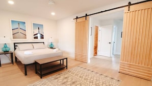 A bedroom with a bed, bedside tables, a bench, a patterned rug, and a sliding door.