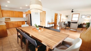 A spacious kitchen with wooden cabinets, a large dining table, and a modern chandelier.