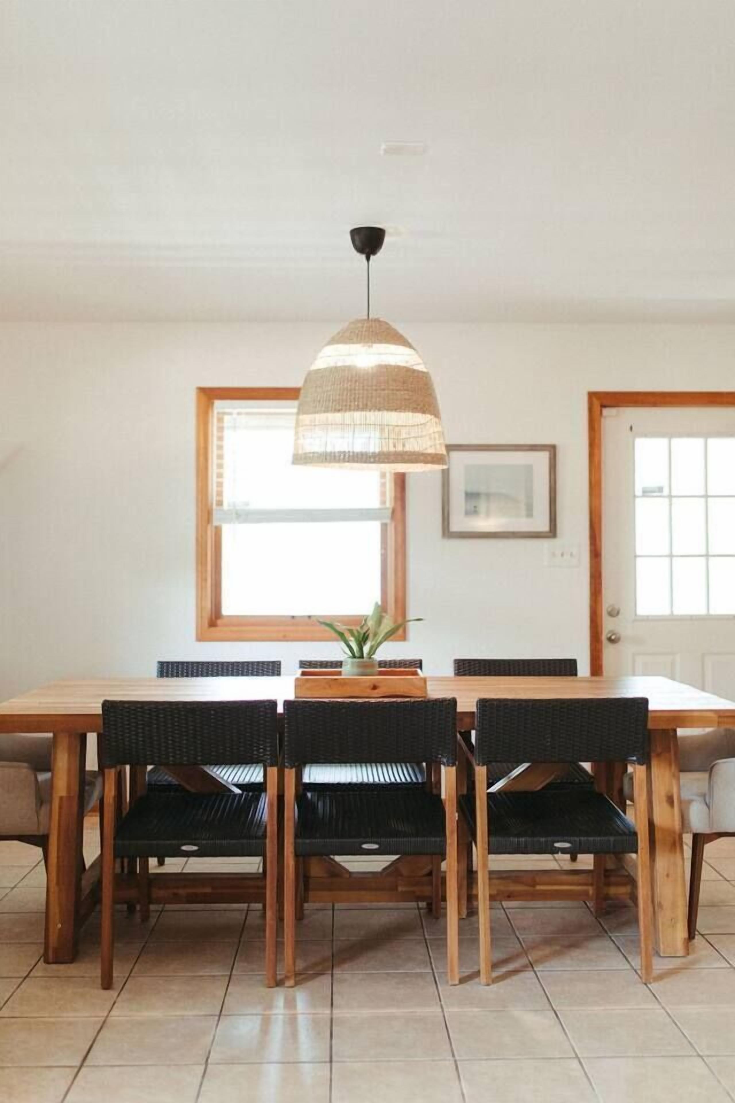 Zona pranzo con tavolo e sedie in legno, lampadario e finestra con persiane.