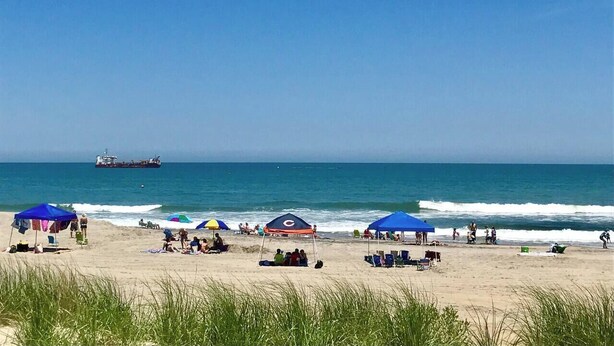 A beach with umbrellas, people, and a ship in the distance.