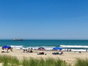 A beach with umbrellas, people, and a ship in the distance. - Classic Duck Cottage – Heated Pool + Walk to Beach (Duck)