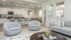 A modern living room with a grey sofa, two armchairs, a coffee table, and a dining area in the background. - GOODE.HOMES | Luxury Modern Home w/ pool/spa (Santa Clarita)