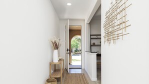 A hallway with a wooden floor, a woven rug, a basket, a vase with dried flowers, and a wall-mounted wooden art piece. - GOODE.HOMES | Luxury Modern Home w/ pool/spa (Santa Clarita)