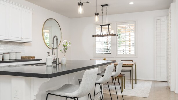 A modern kitchen with a large island, bar stools, pendant lighting, and a view of the outdoors through the window. - GOODE.HOMES | Luxury Modern Home w/ pool/spa (Santa Clarita)