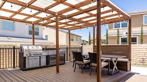 An outdoor patio with a wooden pergola, a barbecue grill, and two wicker chairs. - GOODE.HOMES | Luxury Modern Home w/ pool/spa (Santa Clarita)