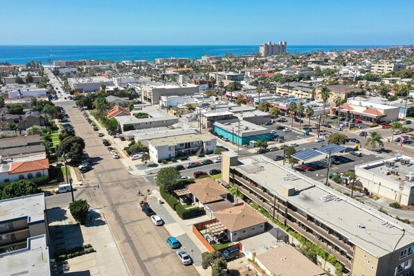 An aerial view of a coastal city with a mix of residential and commercial buildings, a clear blue sky, and the ocean in the background.