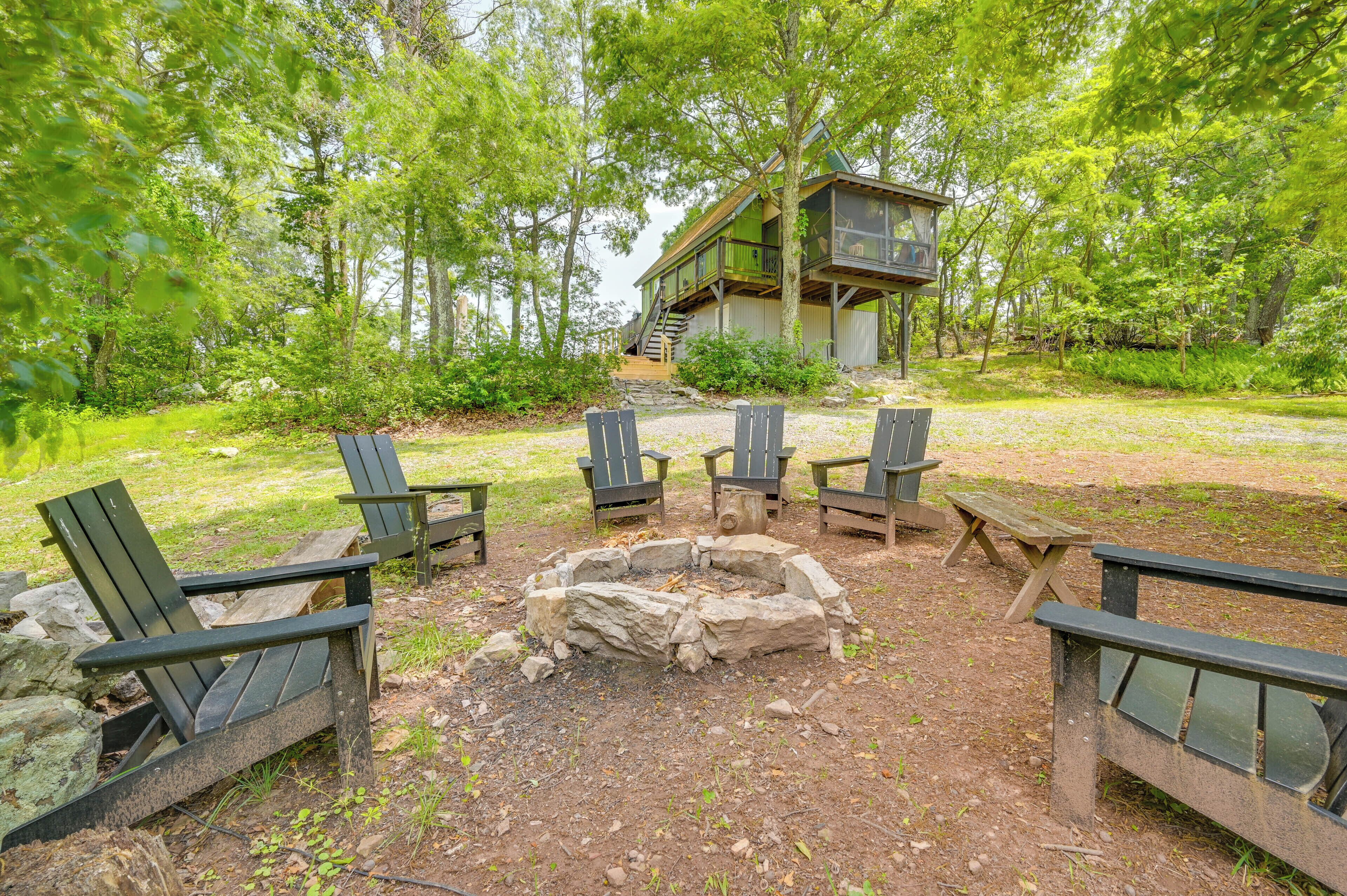 Une cabane dotée d’une terrasse, entourée d’un foyer et de chaises Adirondack, située dans une zone boisée.