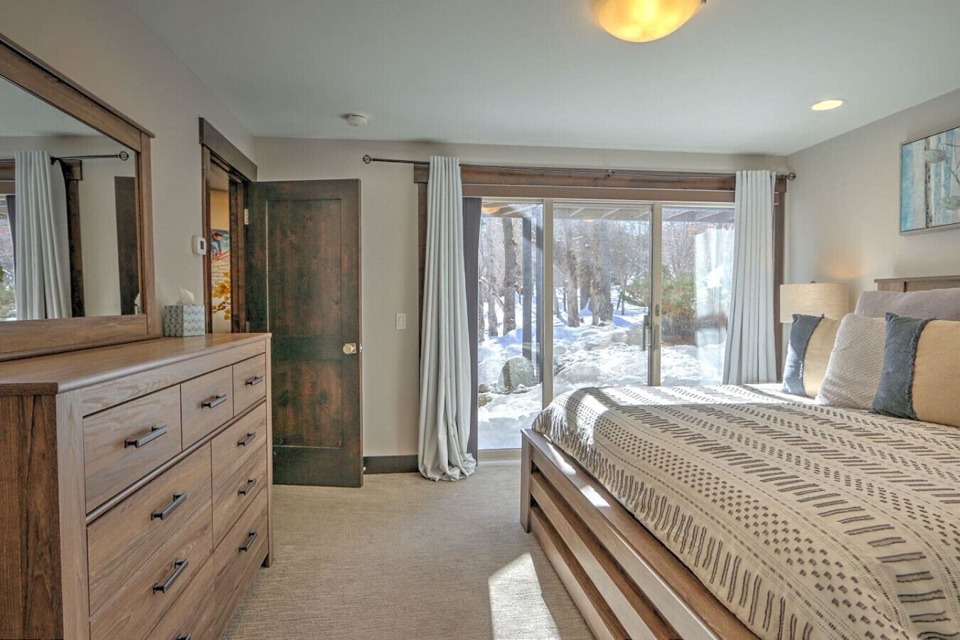 Une chambre avec un grand lit, une commode en bois et une porte-fenêtre coulissante donnant sur un espace extérieur enneigé.