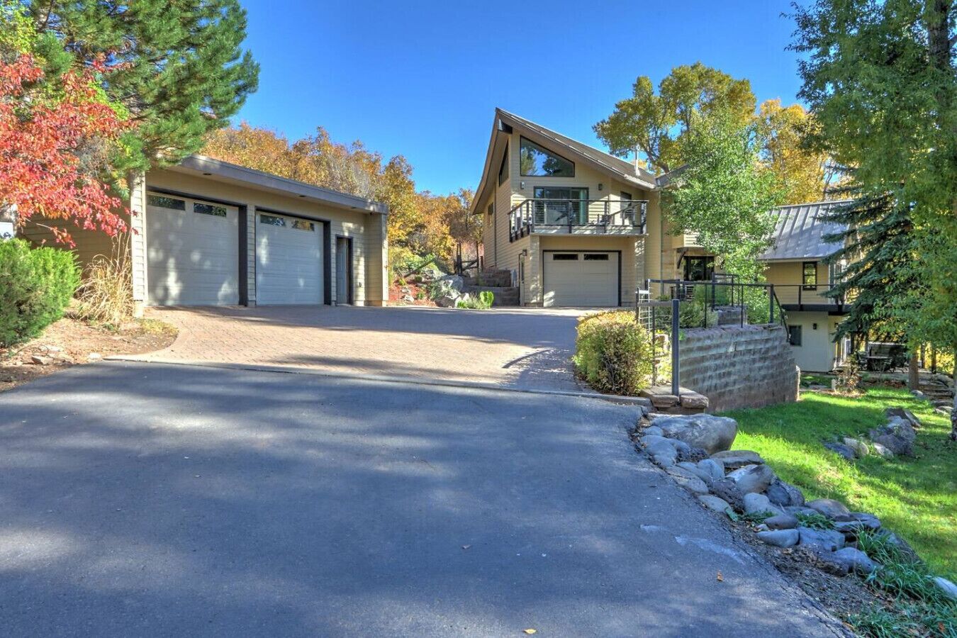 Une maison à deux étages avec un garage, une allée couverte et un mur de soutènement en pierre.