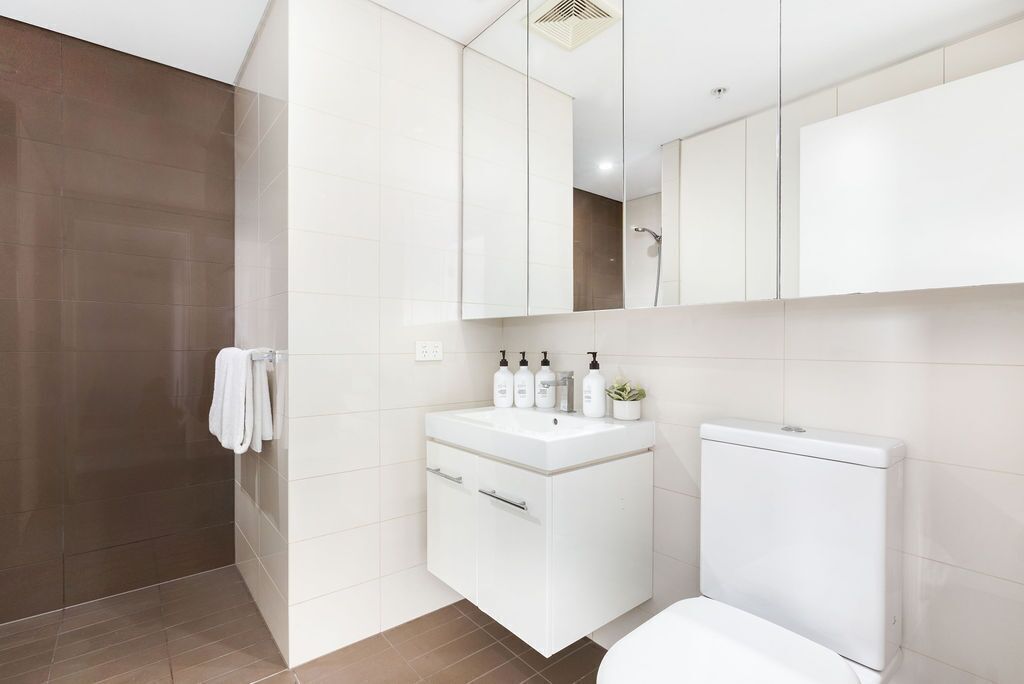 Un baño moderno con ducha, lavamanos y artículos de aseo, y un inodoro.