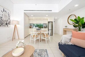 A modern living room with a sofa, a coffee table, and a dining area with chairs and a table. - The Alta Apartments by Urban Rest (Surry Hills)