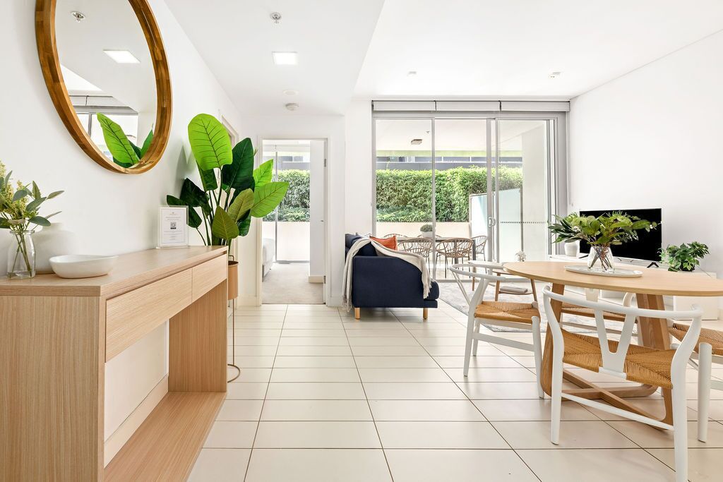 A modern kitchen with a wooden counter, a round dining table with white chairs, and a large window offering a view of the outdoors.