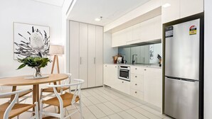 A modern kitchen with white cabinetry, a stainless steel refrigerator, and a dining area with a round table and chairs. - The Alta Apartments by Urban Rest (Surry Hills)