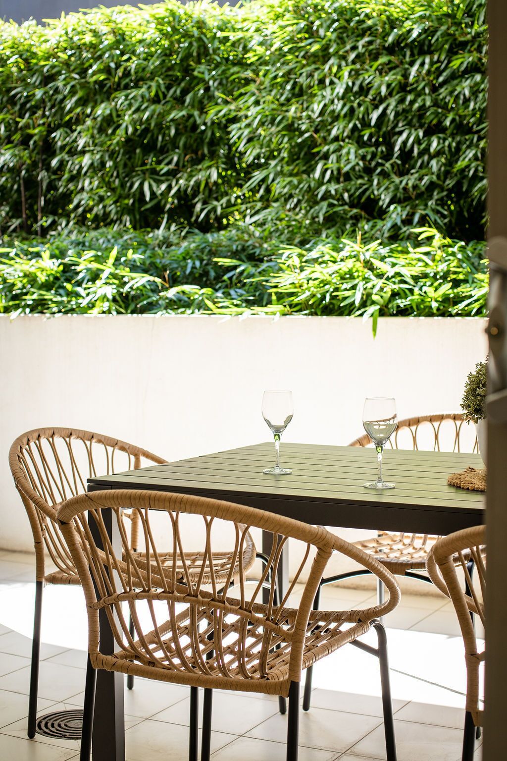 A dining area with a table and chairs, a hedge in the background, and a view of the sky.
