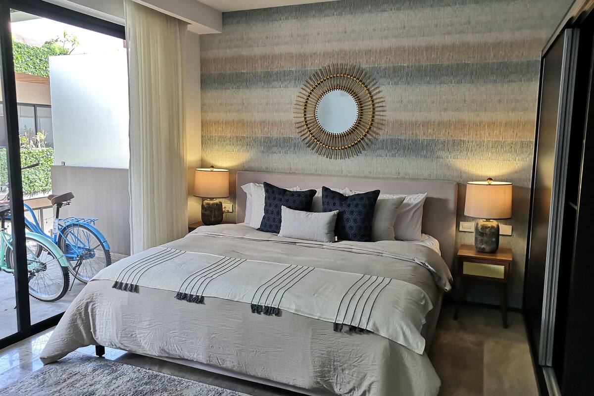 A hotel room with a large bed, two bedside lamps, a wall-mounted mirror, and a bicycle outside the window.