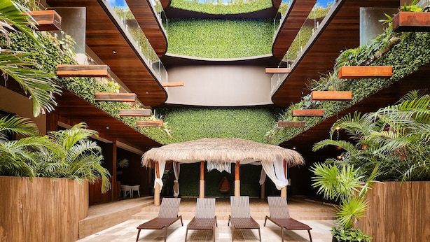 A modern indoor pool area with a thatched umbrella, wooden lounge chairs, and lush greenery. - Menesse Tulum by Spot Rentals (Tulum)