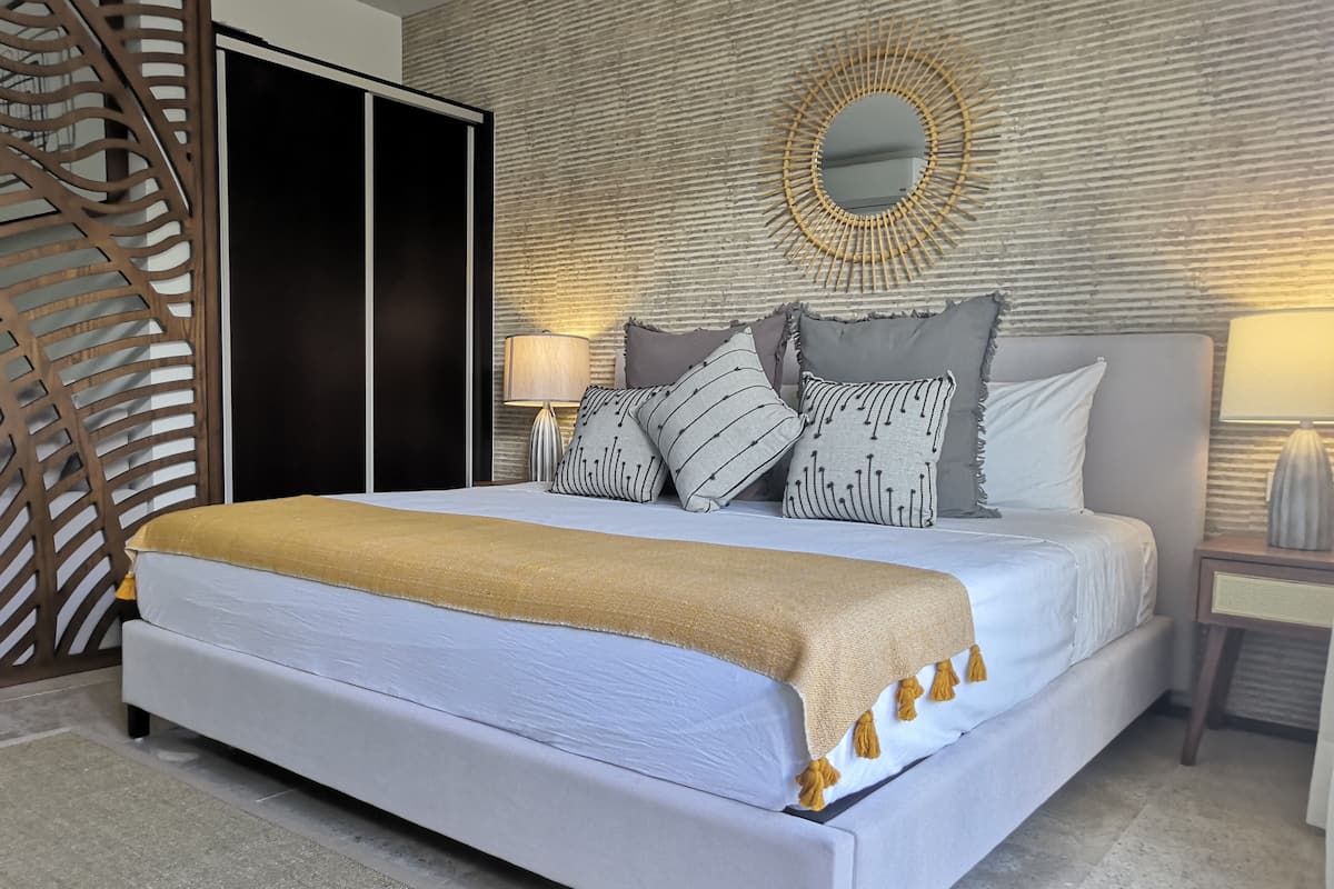 A neatly made bed with a white and gold blanket, a headboard with a mirror, and a wall with a textured pattern.