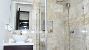 Un baño moderno con ducha de vidrio, lavamanos blanco y protector contra salpicaduras de mármol.