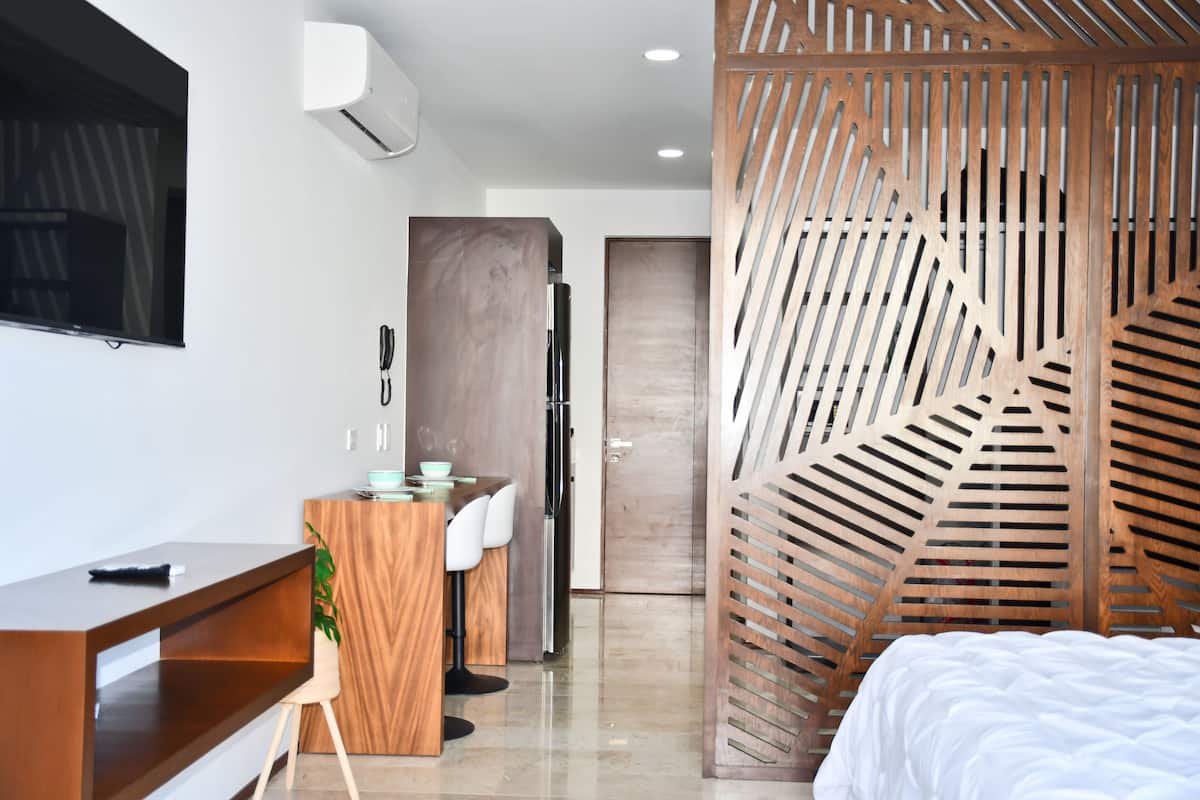 A modern hotel room with a wooden desk, a bed, and a large window.