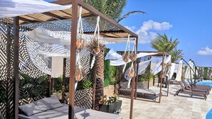 A poolside area with lounge chairs, a pergola with macrame decorations, and a clear blue sky. - Menesse Tulum by Spot Rentals (Tulum)