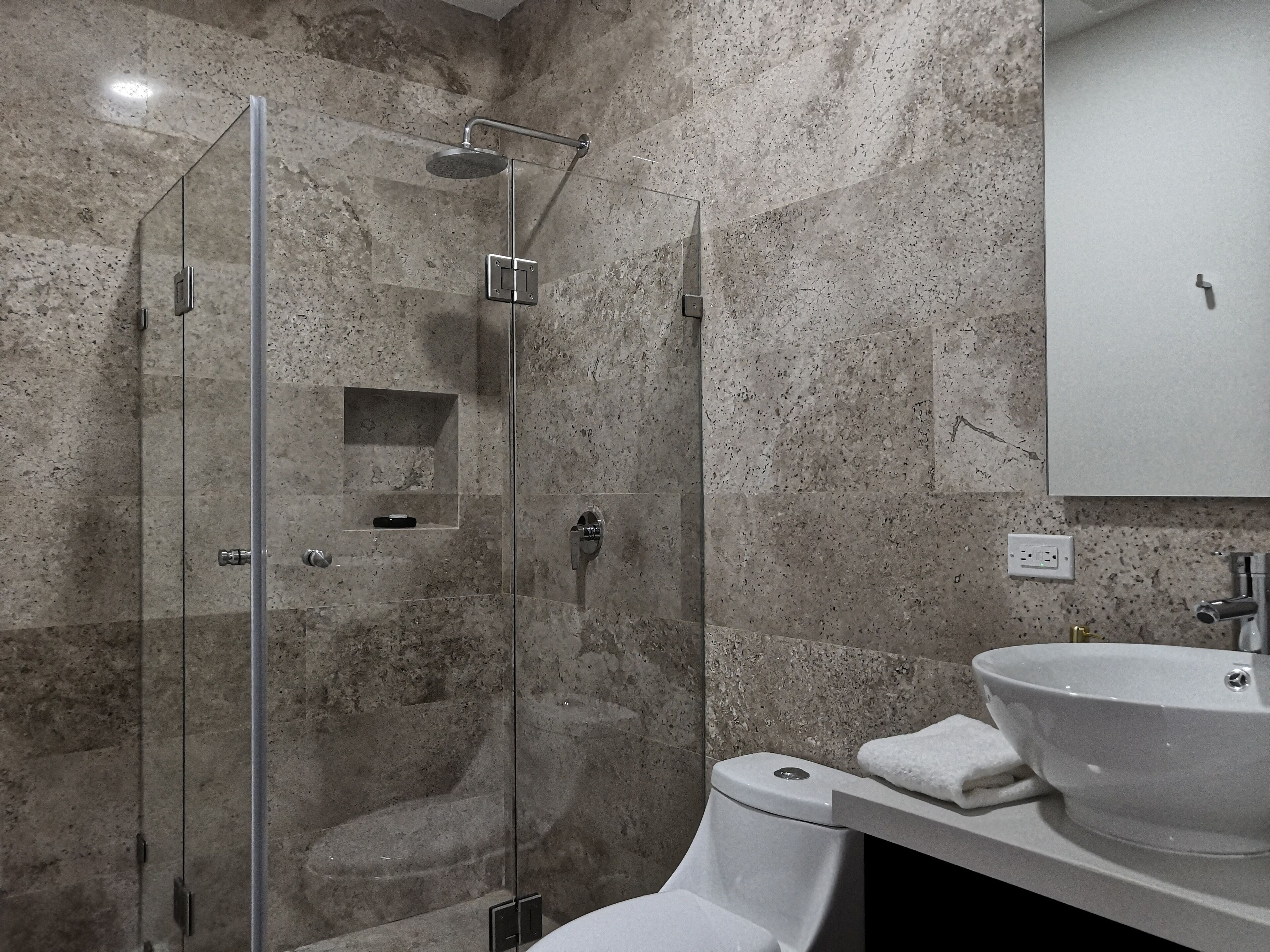 Un bagno moderno con cabina doccia in vetro, un lavandino bianco e una parete rivestita in marmo.