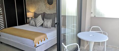 A bedroom with a bed, a bedside table, a chair, and a view of the outside.