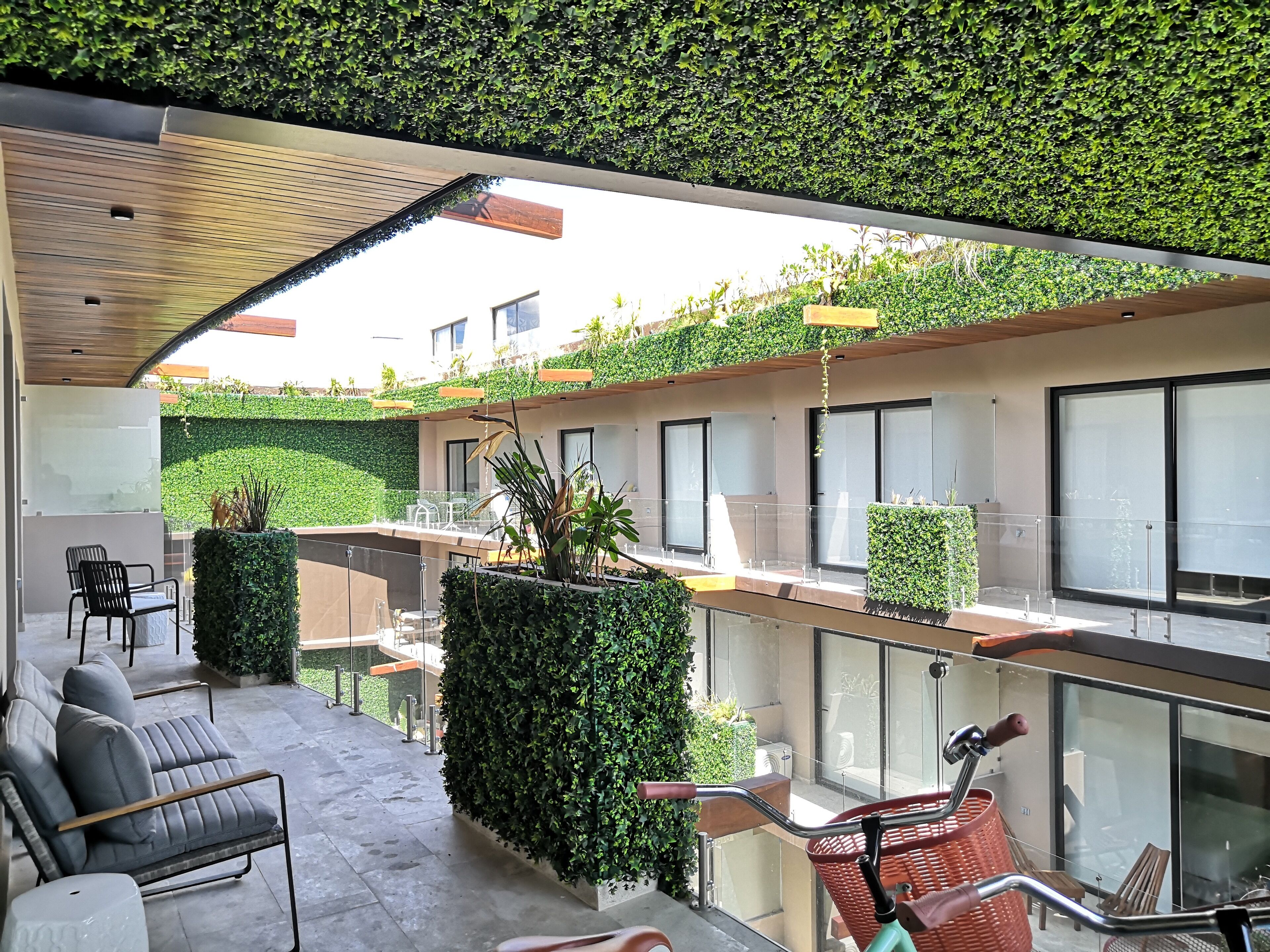 A modern outdoor seating area with a glass balustrade, a wooden ceiling, and lush green plants.