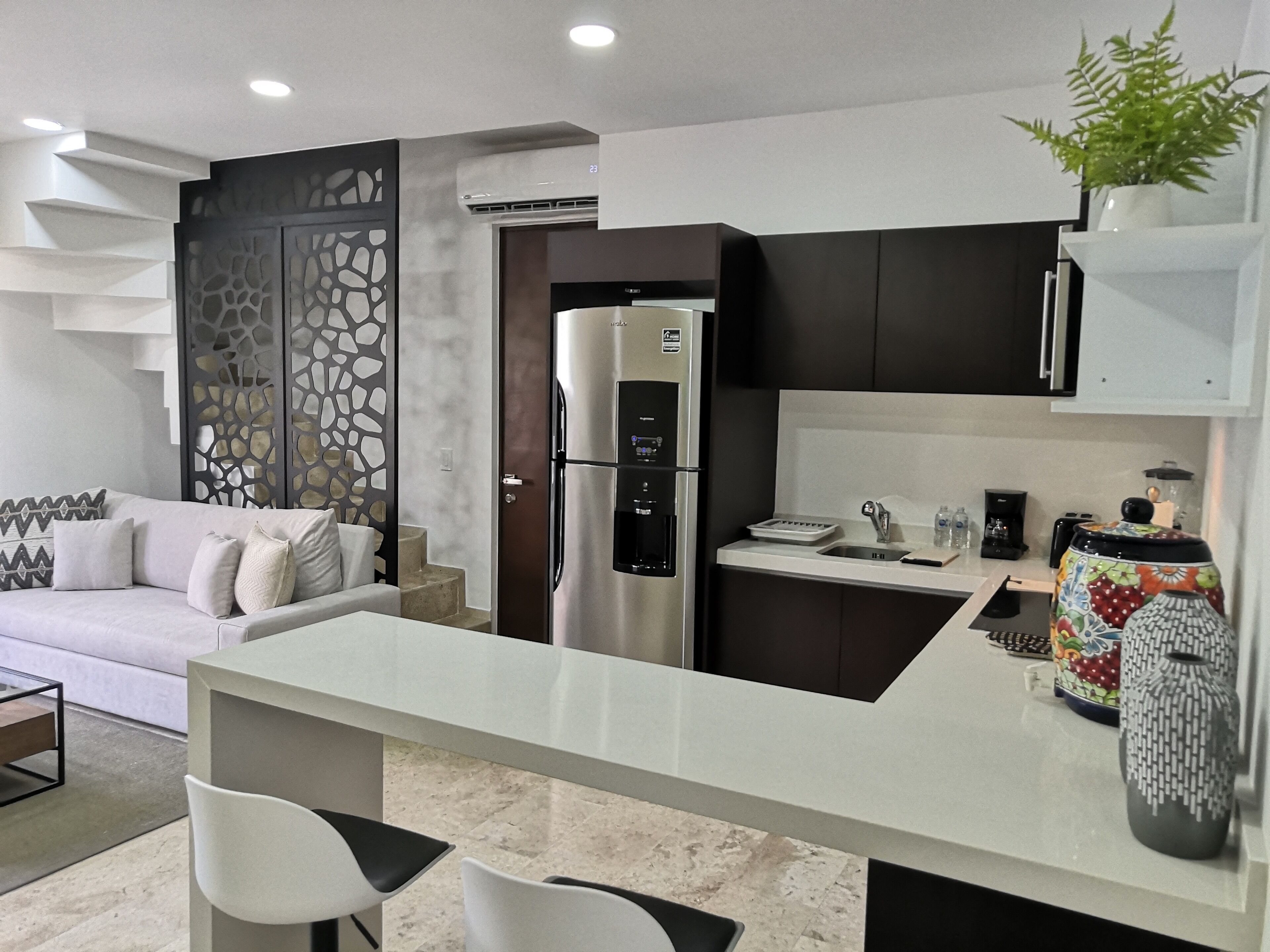 Una cocina moderna con refrigerador empotrado, una encimera blanca y un área de comedor con dos sillas.