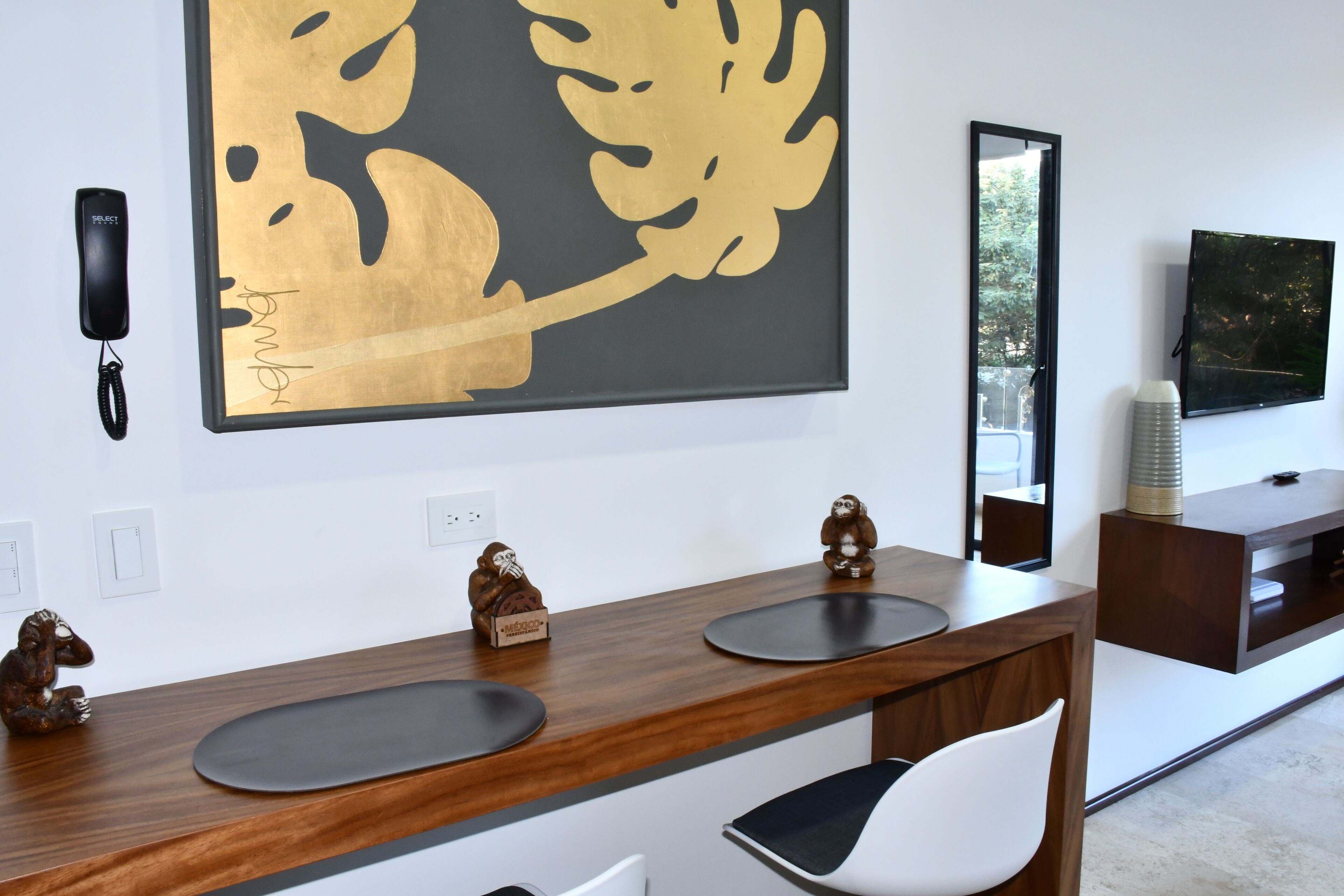 A modern hotel room with a wooden vanity, a large abstract gold and black artwork, a mounted telephone, and a flat-screen TV on a wooden console.