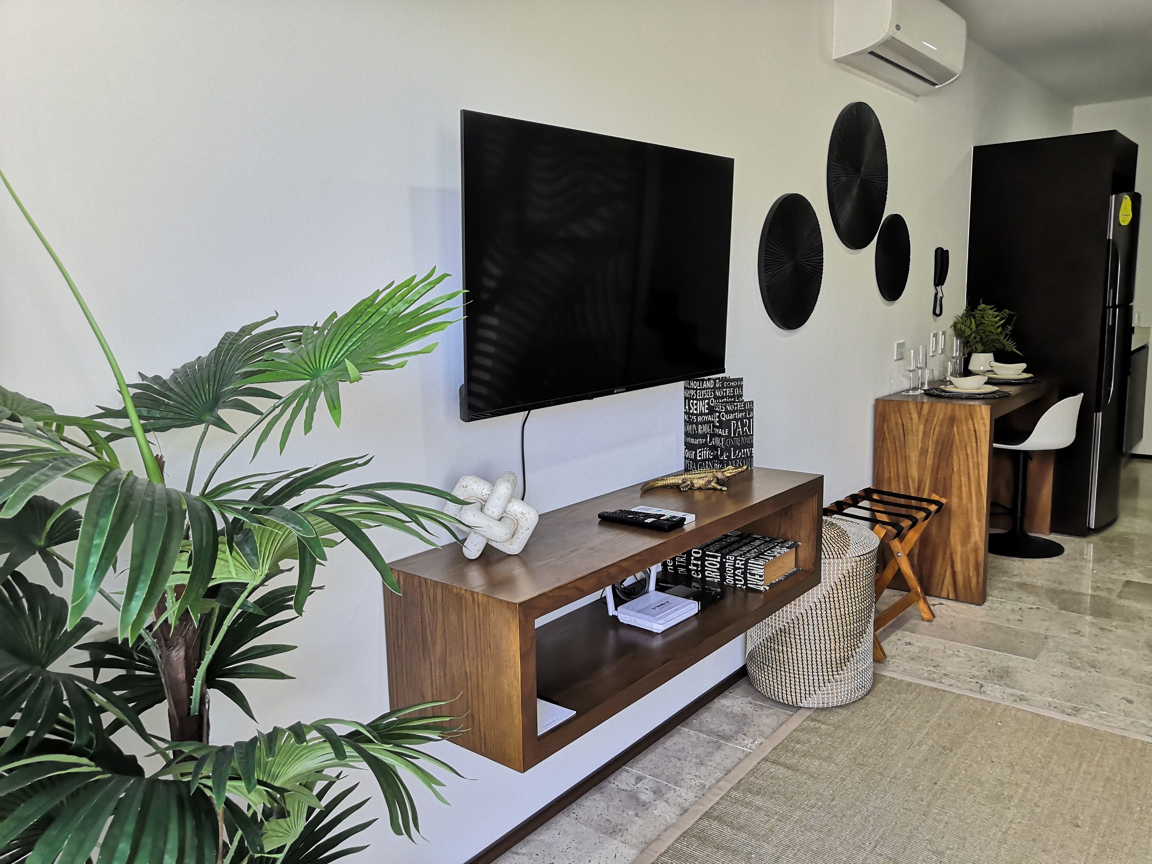 Un salon moderne avec un téléviseur à écran plat, un meuble de rangement en bois et une plante en pot.