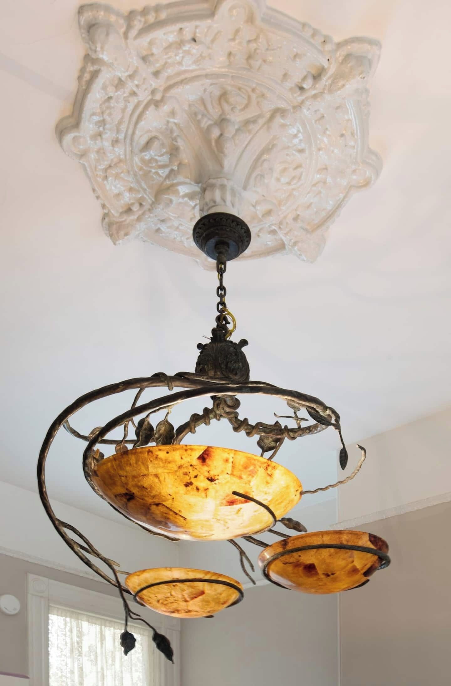 A chandelier with a rustic design, featuring a central globe and two smaller globes, suspended from an ornate ceiling medallion.