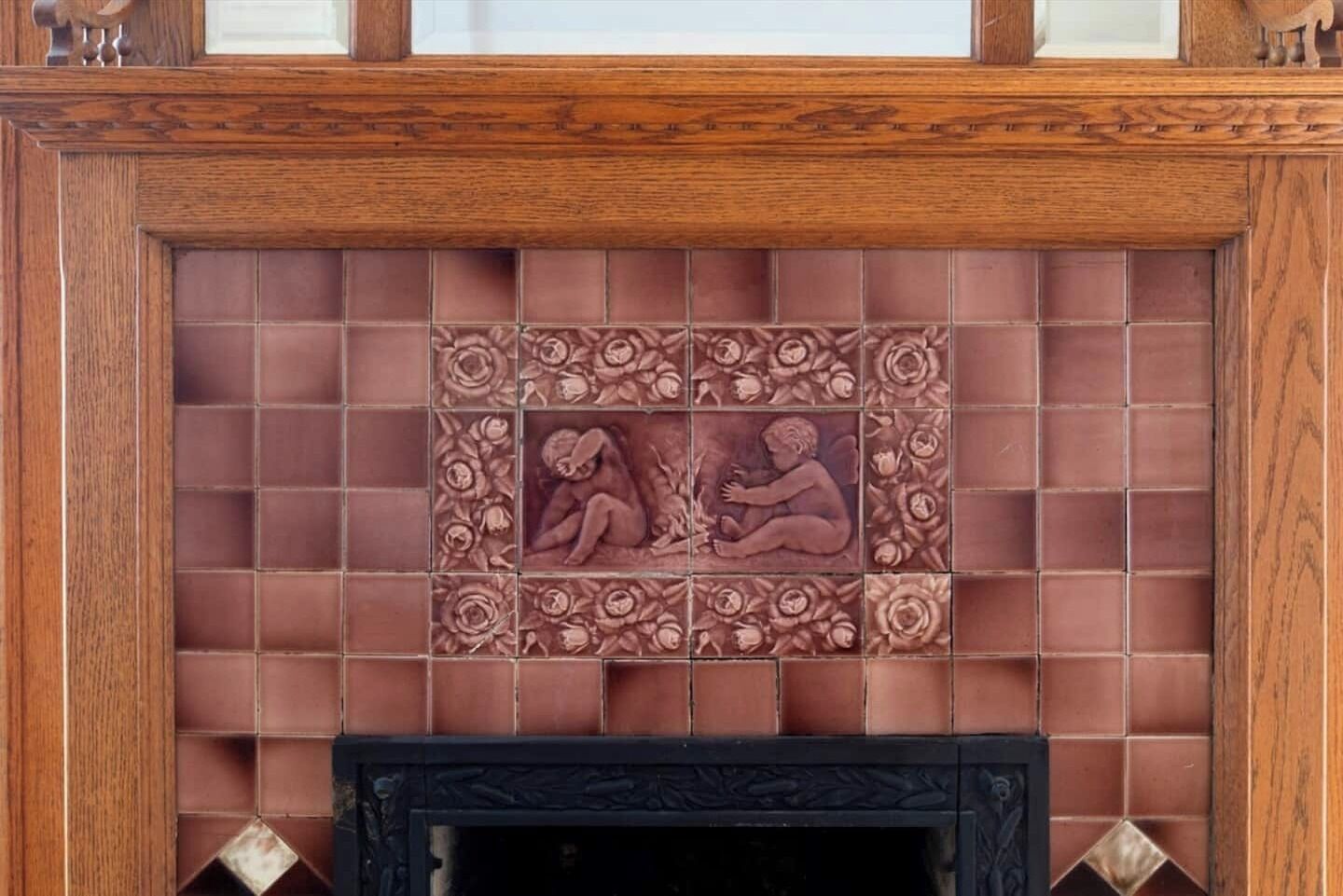 A fireplace with a tiled surround featuring floral and human motifs.