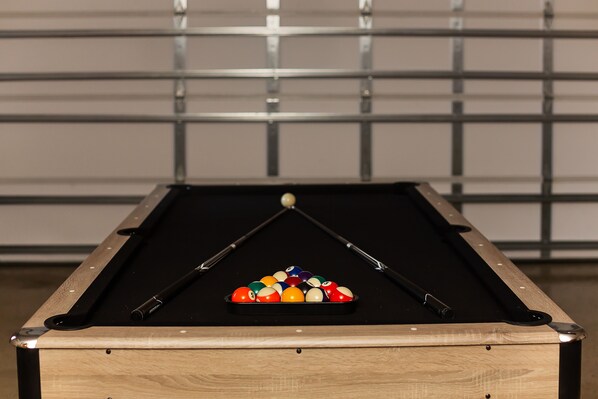 A pool table with a triangular rack of billiard balls, a cue stick, and a white ball in the center.