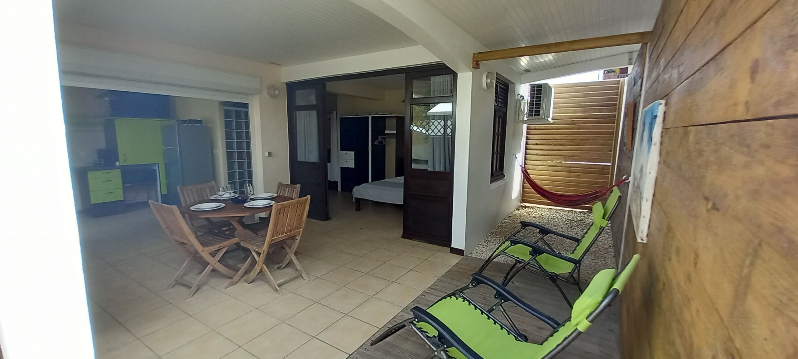 A hotel room with a dining area, a bed, and a balcony with a hammock.