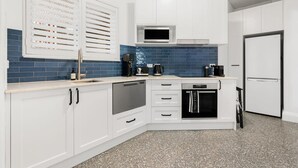A modern kitchen with white cabinets, a microwave, a dishwasher, and a refrigerator. - Coogee Riviera in Coogee (Coogee)