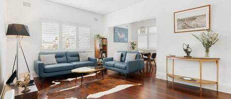 A modern living room with a blue sofa set, a coffee table, a wooden floor, and a ceiling fan.
