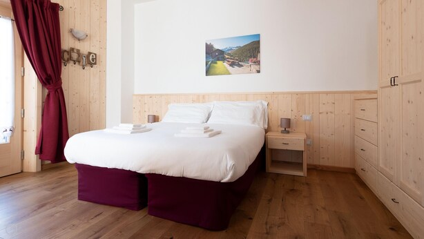 A bedroom with a wooden floor, a bed with white linens, a nightstand with a lamp, and a wooden wardrobe. - Italianway - Ripa Fontana 1 Mono (Valdidentro)