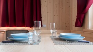 A wooden dining table with blue plates and clear glasses, set against a wooden wall with red curtains. - Italianway - Ripa Fontana 1 Mono (Valdidentro)