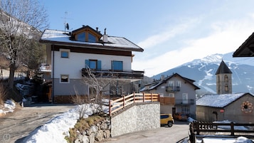 A two-story building with a balcony, a stone wall, and a mountain backdrop.