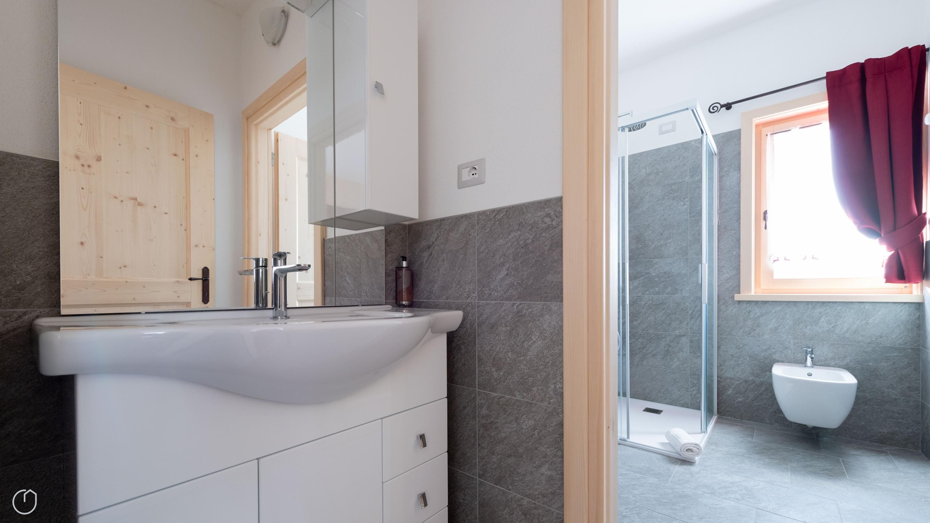 Un baño moderno con un lavabo blanco, cabina de ducha con vidrio y un bidé.