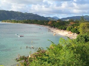 A beach with clear water, a sandy shore, and a backdrop of hills.