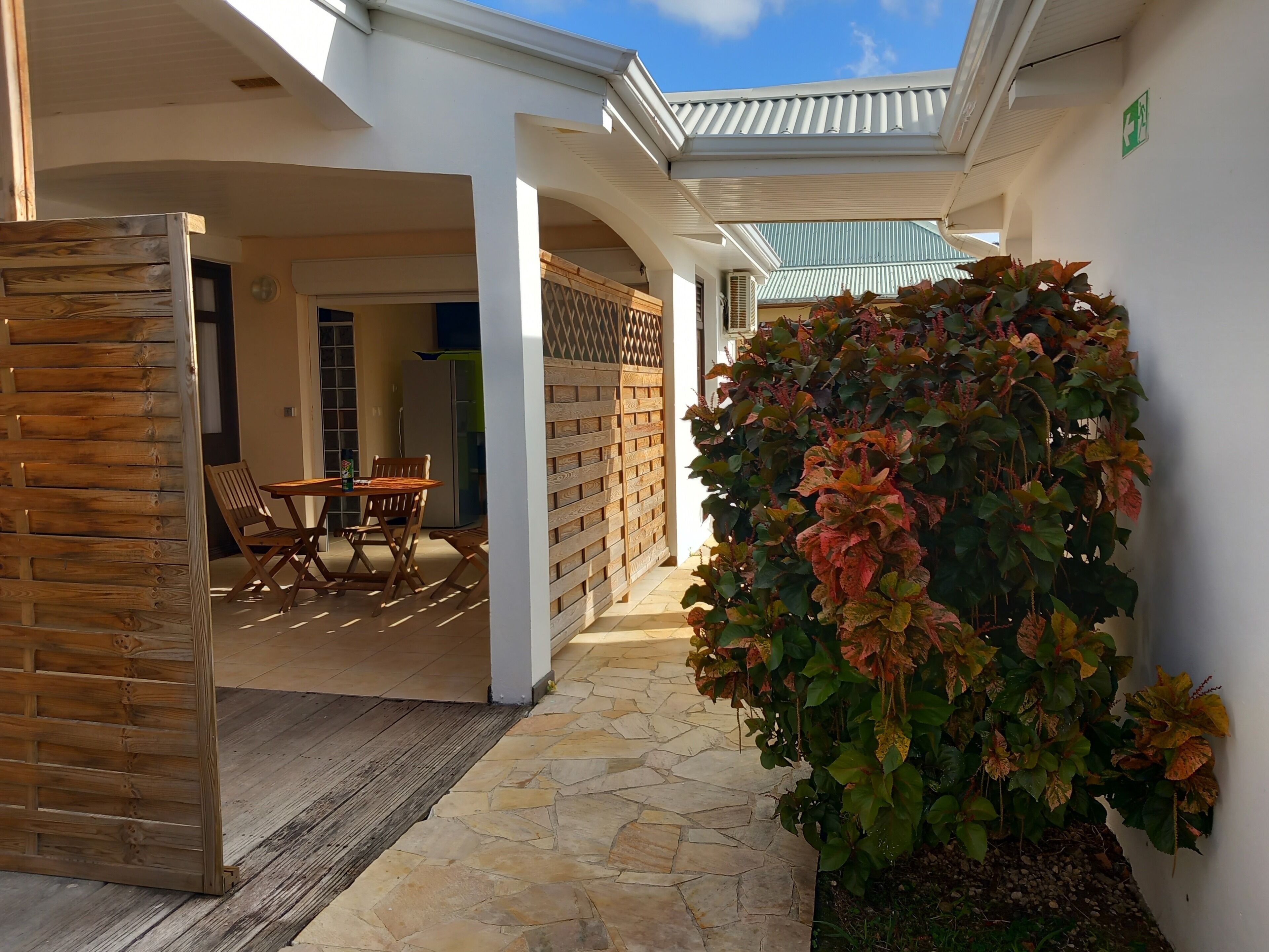 A covered outdoor area with a wooden table and chairs, a stone pathway, and a wall-mounted plant.