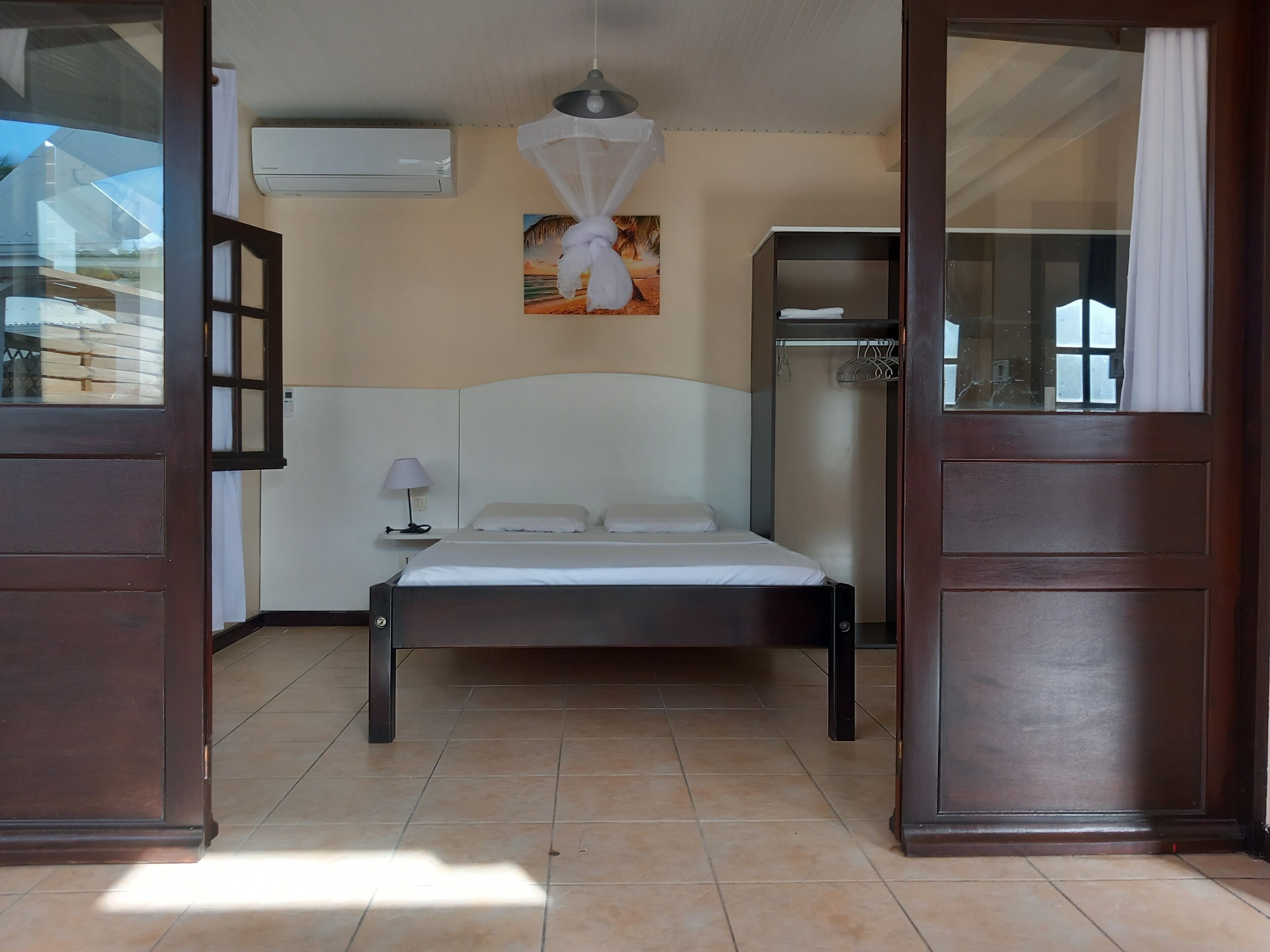 Une chambre à coucher comprenant un lit, une table de chevet, une lampe, un appareil de climatisation, un tableau et une armoire.