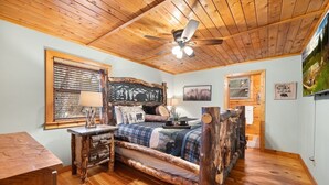 A rustic bedroom with a wooden bed, a ceiling fan, and a large window with blinds. - Creekfront: Views, Hot Tub, Fire Pit & Game Room (Blue Ridge)