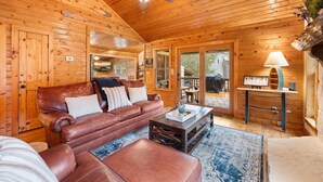 A cozy cabin interior with a leather sofa, a coffee table, and a ceiling fan. - Creekfront: Views, Hot Tub, Fire Pit & Game Room (Blue Ridge)